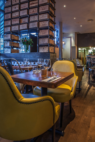 Contemporary restaurant interior with yellow, studded, upholstered chairs and bespoke industrial shelving with reclaimed wine box drawers