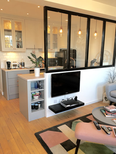 Open plan living area with painted grey kitchen and glazed room divider on which a TV is mounted