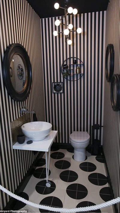 Lavatory with bowl sink on a freestanding vanity shelf, gold glass, splashback tiles, black and gold convex wall mirrors, spotty floor tiles and stripy wallpaper and black toilet roll holder with black toilet paper