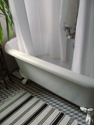 White and grey roll top bath with claw feet, 3D effect moroccan cement floor tiles in black, grey and white, with white shower curtains and vintage mixer tap