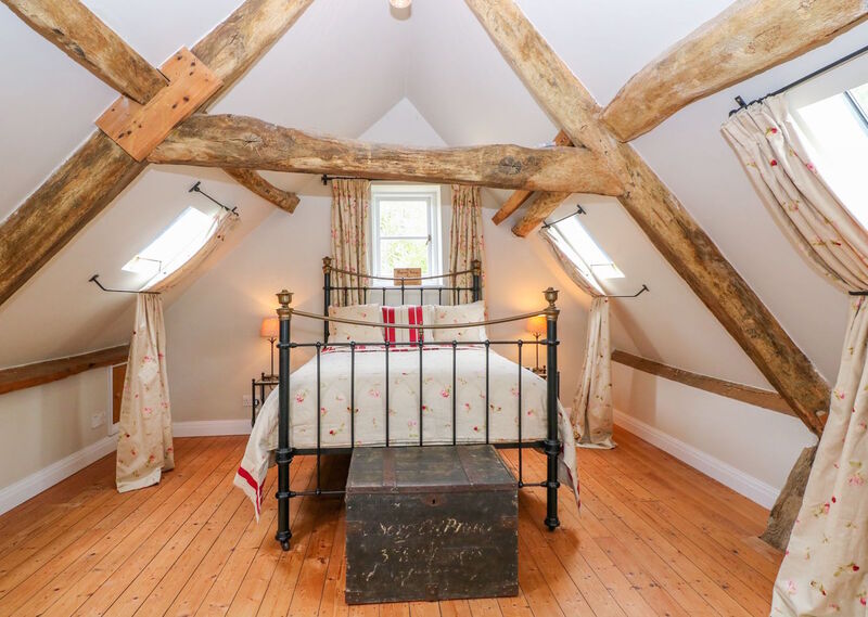 Pretty, feminine attic room with original Oak rafters and a black and gold, traditional, metal bed with ditsy, floral bedcovers and matching curtains