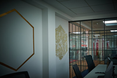 Minimal white office desks in an open plan office with glass, crittal-style partition walls and gold graffiti