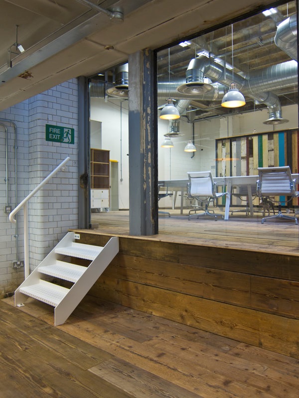 Office with brick tiled walls, reclaimed wooden floors, sleek white Modus desks, Eames chairs and exposed ducting system