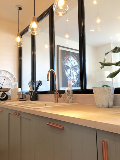 Painted, grey kitchen cabinets, with white oiled, oak worktop a half glazed room divider and three exposed bulb pendant lights