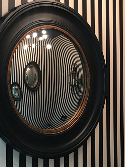 Black and gold convex mirror from Graham and Green, reflecting black and white stripy walls and two convex mirrors