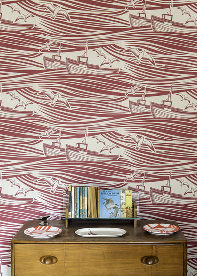 Vintage drawers and books stand in front of red and white Whitby wallpaper which features trawlers, seagulls and waves by Mini Moderns
