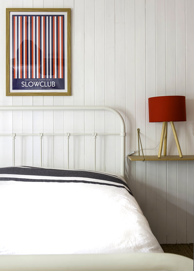Nautical style tongue and groove clad walls with white metal bedposts and Slowclub poster