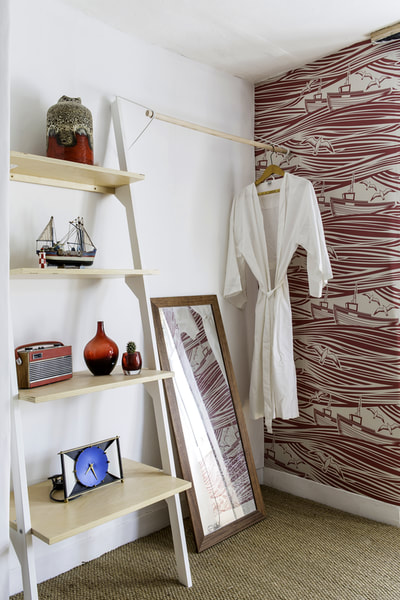 Simple, open, white and wood wardrobe and white dressing gown with open shelves holding vintage ornaments and radio